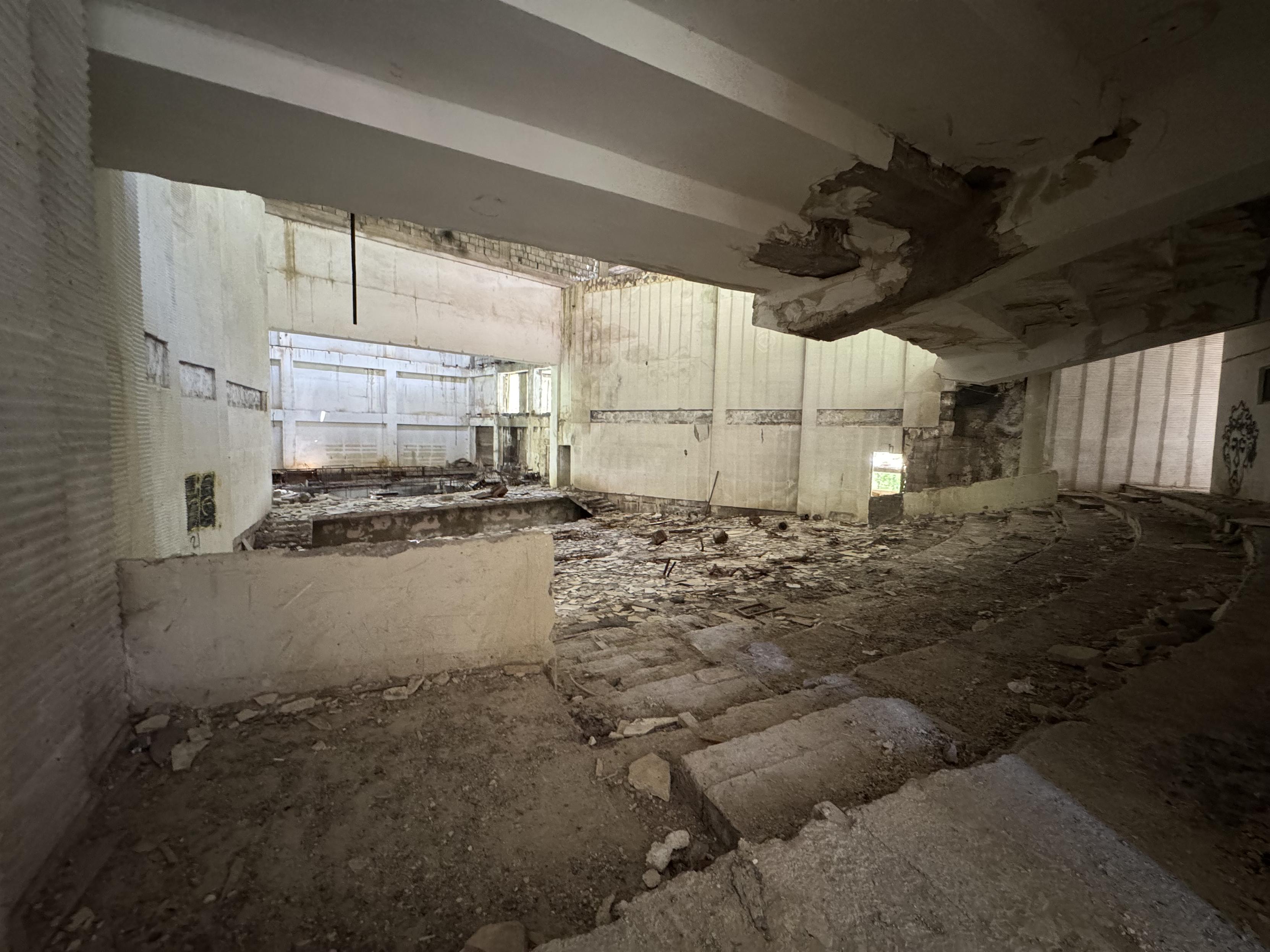 Blick in einen Kino- oder Theatersaal. Hinten die Bühne, davor Reste von Stufen zu erkennen, die früher bestuhlt waren.